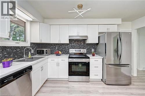 Modern kitchen featuring white cabinetry, stainless steel appliances, a mosaic tile backsplash, light-toned countertops, and wood-finish flooring - 92 Pinemeadow Crescent, Waterloo, ON - Indoor Photo Showing Kitchen With Double Sink
