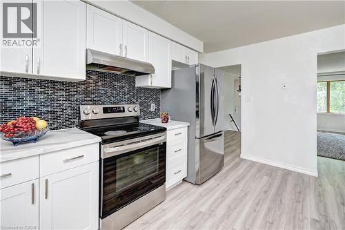 Kitchen featuring white cabinetry, a dark mosaic tile backsplash, stainless steel appliances, white countertops, and light wood-finish flooring - 92 Pinemeadow Crescent, Waterloo, ON - Indoor Photo Showing Kitchen With Upgraded Kitchen