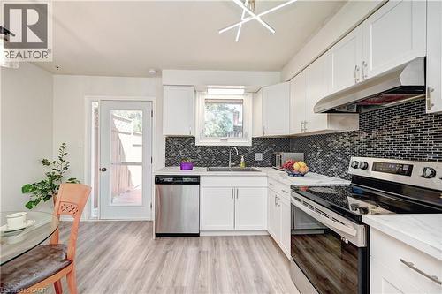 Kitchen featuring white cabinetry, a dark mosaic tile backsplash, stainless steel appliances, light wood-finish flooring, and white countertops - 92 Pinemeadow Crescent, Waterloo, ON - Indoor Photo Showing Kitchen With Upgraded Kitchen