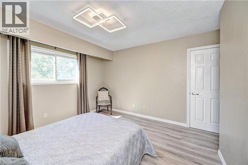 Spacious room featuring wood-finish flooring, a contemporary ceiling light fixture, a paneled door with brushed nickel hardware, and a window with natural light - 92 Pinemeadow Crescent, Waterloo, ON - Indoor Photo Showing Bedroom