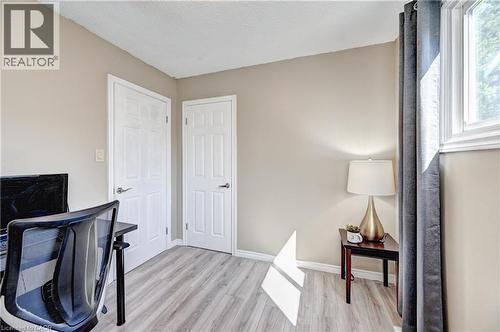 Light wood-finish flooring complements the neutral wall color in this room featuring two white paneled doors, a white-framed window, and white baseboards - 92 Pinemeadow Crescent, Waterloo, ON - Indoor