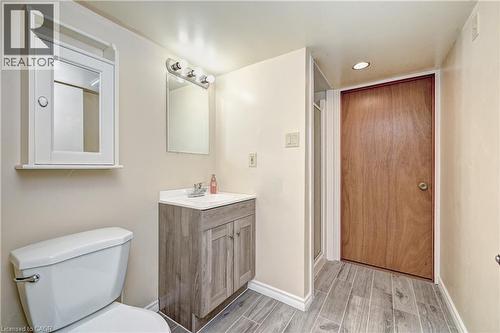 Bathroom featuring a wood-finish vanity with an integrated sink, a wall-mounted mirror, overhead vanity lighting, a medicine cabinet, and wood-look tile flooring - 92 Pinemeadow Crescent, Waterloo, ON - Indoor Photo Showing Bathroom