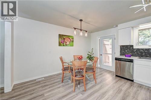 Open-concept kitchen and dining area featuring wood-finish flooring, crisp white cabinetry, dark mosaic tile backsplash, and stainless steel dishwasher - 92 Pinemeadow Crescent, Waterloo, ON - Indoor