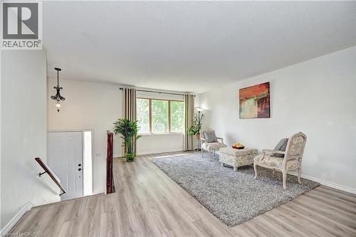 Bright living space featuring wood-finish flooring, a large window with vertical blinds, and a white entry door with a vertical window pane - 92 Pinemeadow Crescent, Waterloo, ON - Indoor