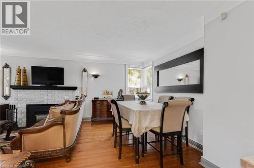 Open-concept living and dining area featuring rich wood-finish flooring, a white brick fireplace with a black mantel, and crown molding - 1 Galbraith Drive, Hamilton, ON - Indoor Photo Showing Dining Room With Fireplace