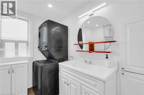 Laundry area featuring a stacked washer and dryer, white vanity with integrated sink, circular mirror with accent shelving, and recessed lighting - 1 Galbraith Drive, Hamilton, ON - Indoor Photo Showing Laundry Room