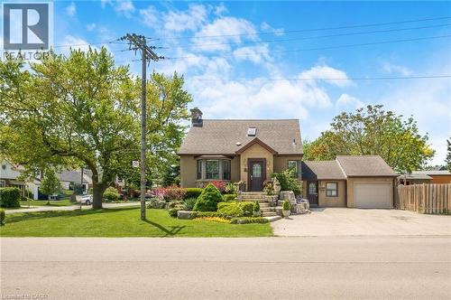Stucco exterior residence featuring a detached single-car garage, mature front yard landscaping with tiered stone elements, and a paved driveway - 1 Galbraith Drive, Hamilton, ON - Outdoor With Facade