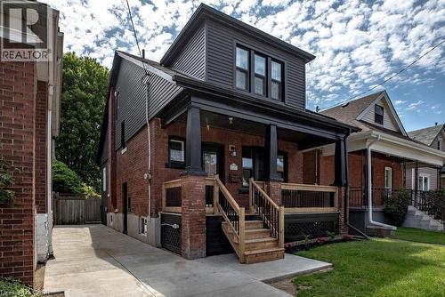 Brick and dark siding exterior with a covered front porch featuring dark columns and trim - 106 Grosvenor Avenue N, Hamilton, ON - Outdoor