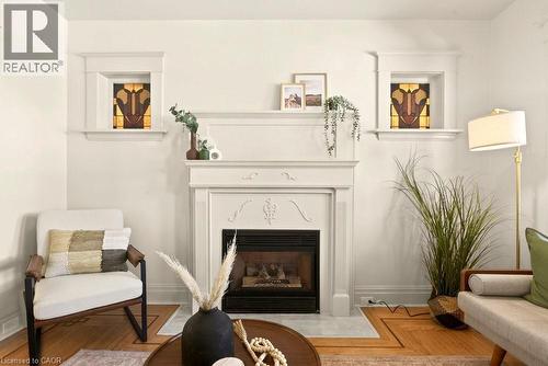 Fireplace with ornate mantel and hearth, flanked by two framed stained-glass transom windows - 106 Grosvenor Avenue N, Hamilton, ON - Indoor Photo Showing Living Room With Fireplace