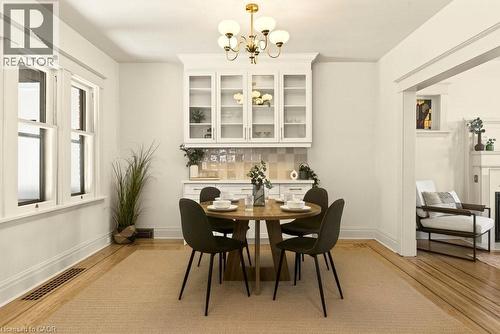 Dining area featuring hardwood flooring, built-in cabinetry with glass fronts, a tile backsplash, and a gold-finish chandelier - 106 Grosvenor Avenue N, Hamilton, ON - Indoor Photo Showing Dining Room