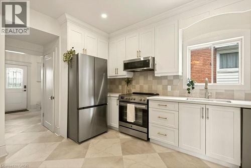 Kitchen featuring white shaker-style cabinetry with gold-tone hardware, stainless steel appliances, a checkered tile backsplash, and light-toned countertops - 106 Grosvenor Avenue N, Hamilton, ON - Indoor Photo Showing Kitchen