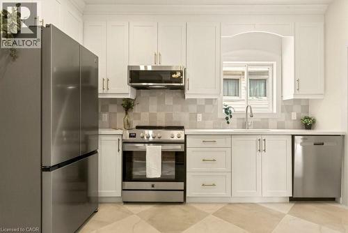 Kitchen featuring white shaker-style cabinetry with gold-toned hardware, stainless steel appliances, and light-toned countertops - 106 Grosvenor Avenue N, Hamilton, ON - Indoor Photo Showing Kitchen With Upgraded Kitchen