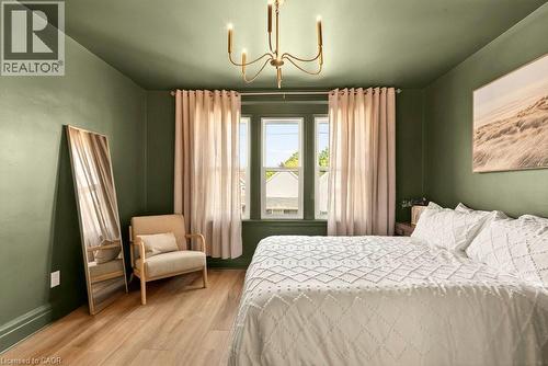 Room featuring wood-finish flooring, a multi-pane window, and a contemporary chandelier - 106 Grosvenor Avenue N, Hamilton, ON - Indoor Photo Showing Bedroom