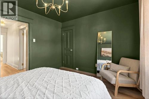 Bedroom featuring dark green walls and ceiling, a gold-toned chandelier, and light wood-finish flooring - 106 Grosvenor Avenue N, Hamilton, ON - Indoor Photo Showing Bedroom