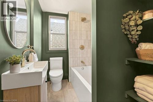Contemporary bathroom featuring a floating wood-finish vanity with an integrated sink, polished brass fixtures, and a curved mirror - 106 Grosvenor Avenue N, Hamilton, ON - Indoor Photo Showing Bathroom