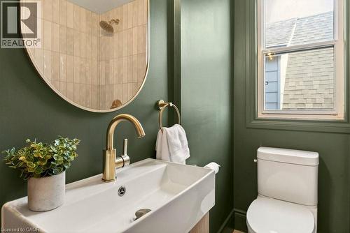 Bathroom featuring a rectangular vessel sink with a gold-tone faucet, a gold-framed arched mirror, and a white toilet - 106 Grosvenor Avenue N, Hamilton, ON - Indoor Photo Showing Bathroom