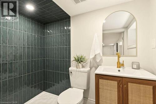 Bathroom with vertical-set teal tile shower, white toilet, and wood-finish vanity with woven cabinet fronts - 106 Grosvenor Avenue N, Hamilton, ON - Indoor Photo Showing Bathroom