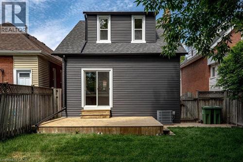 Rear exterior featuring dark horizontal siding, a dormer with two windows, a sliding glass door, a wooden deck, and a grass lawn - 106 Grosvenor Avenue N, Hamilton, ON - Outdoor With Exterior