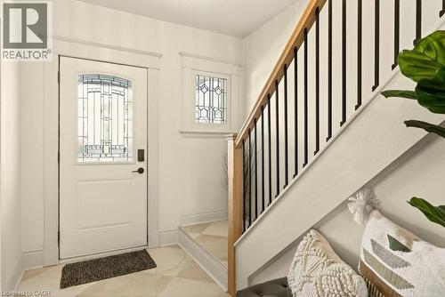 Entryway featuring a white door with decorative glass, complementary transom window, light-toned tiled flooring, and a staircase with wood handrail and black balusters - 106 Grosvenor Avenue N, Hamilton, ON - Indoor Photo Showing Other Room