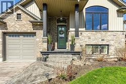 The property features a brick and stone facade, a beige panel garage door with windows, and an arched window on the upper level - 