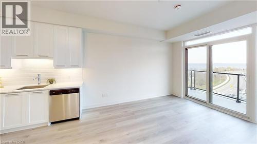 Open-concept living area featuring a modern kitchen with white cabinetry and a tile backsplash, wood-finish flooring, and expansive sliding glass doors leading to a balcony - 385 Winston Road Unit# 709, Grimsby, ON - Indoor Photo Showing Kitchen