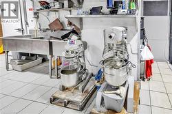 Commercial kitchen space featuring white tiled flooring, stainless steel three-compartment sink, stainless steel shelving, and a white commercial refrigeration unit - 