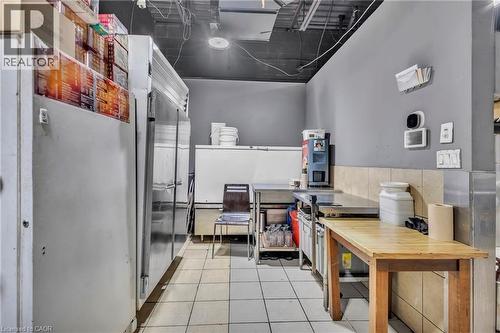 Commercial kitchen space featuring white square floor tiles, light gray walls, exposed ceiling infrastructure, and a wooden-top work table - 402 King Street N, Waterloo, ON 