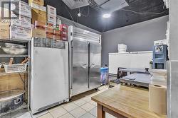 Commercial kitchen space featuring stainless steel refrigeration units, tile flooring, and a wooden work table - 