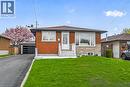 Brick and stone facade bungalow featuring a paved driveway, attached garage, front lawn, and mature flowering tree - 74 Victor Boulevard, Hamilton, ON  - Outdoor 