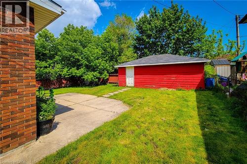 Expansive backyard featuring a detached red shed with a white door and shingled roof, a concrete patio, and a grass lawn - 1 Vera Court, Hamilton, ON - Outdoor