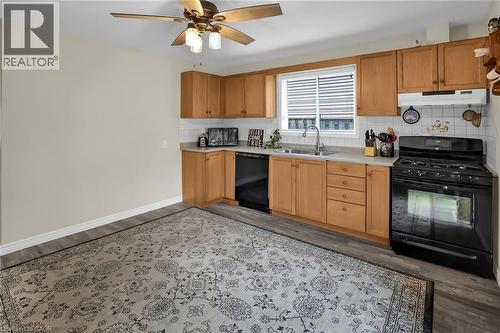 Kitchen with black appliances, under cabinet range hood, light countertops, tasteful backsplash, and wood finished floors - 4432 Dennis Avenue, Beamsville, ON - Indoor Photo Showing Kitchen With Double Sink