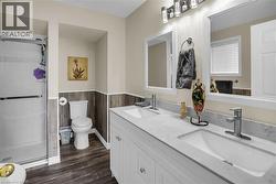 Bathroom featuring wainscoting, double vanity, a stall shower, and wood finished floors - 