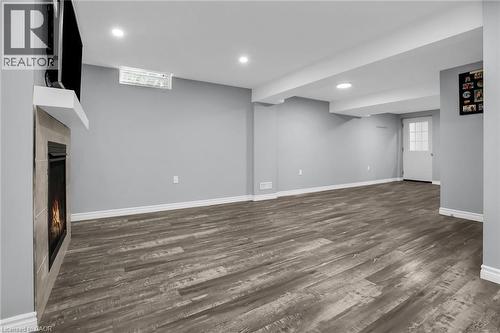 Spacious living room featuring a warm lit fireplace, dark wood flooring, and recessed lighting - 4432 Dennis Avenue, Beamsville, ON - Indoor Photo Showing Basement