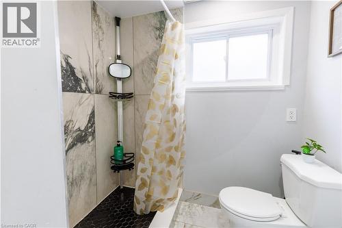Shower with marble-look tile surround and black hexagonal tile flooring, featuring a window with white trim and a white toilet - 18 Silverdale Crescent, London, ON - Indoor Photo Showing Bathroom