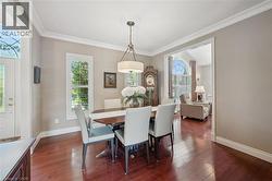 Formal dining area featuring rich wood-finish flooring, crown molding, and a drum pendant light fixture - 