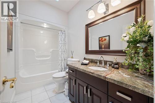 Bathroom featuring a single vanity with a patterned countertop, a built-in tub and shower unit, and white tile flooring - 20 Bonniewood Drive, Drayton, ON - Indoor Photo Showing Bathroom