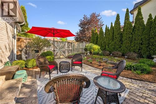 Paved patio area featuring a red sun umbrella, mature privacy trees, a wooden fence, and landscaped garden beds - 20 Bonniewood Drive, Drayton, ON - Outdoor With Deck Patio Veranda