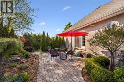 Expansive paver patio with a brick exterior featuring a shingled roofline, and mature landscaping - 