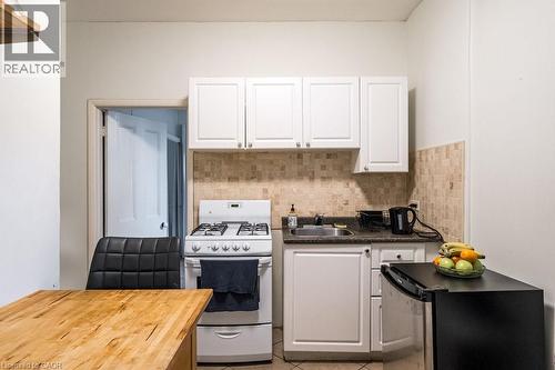 Kitchen featuring white cabinetry, a natural stone tile backsplash, and dark countertops - 95-97 S Fairholt Road S, Hamilton, ON - Indoor Photo Showing Kitchen