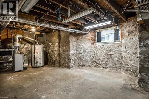 Basement utility area featuring a hot water heater, furnace, concrete flooring, exposed stone foundation walls, and a window - 95-97 S Fairholt Road S, Hamilton, ON - Indoor Photo Showing Basement