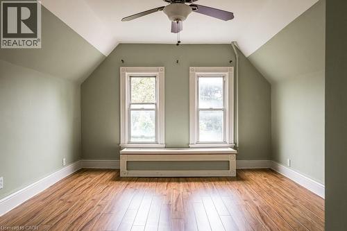 Room featuring wood-finish flooring, two sash windows with detailed trim, a built-in window bench, a ceiling fan, and sloped ceilings - 95-97 S Fairholt Road S, Hamilton, ON - Indoor Photo Showing Other Room