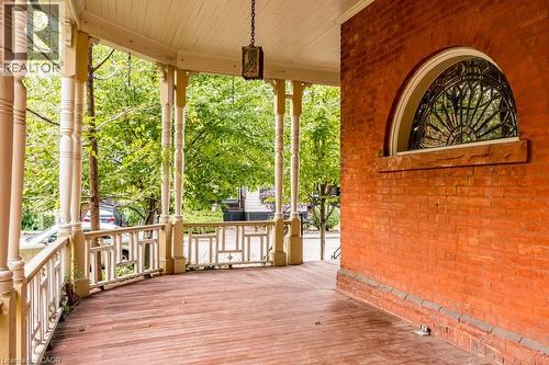 Expansive covered porch featuring wood flooring, decorative railing, turned columns, a ceiling-mounted lantern fixture, and a prominent arched window with intricate metalwork - 95-97 S Fairholt Road S, Hamilton, ON - Outdoor With Deck Patio Veranda With Exterior