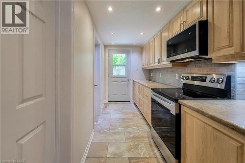 Galley kitchen featuring wood-finish cabinetry, light-toned countertops, and a stone tile backsplash - 319 King Street W, Dundas, ON - Indoor Photo Showing Kitchen