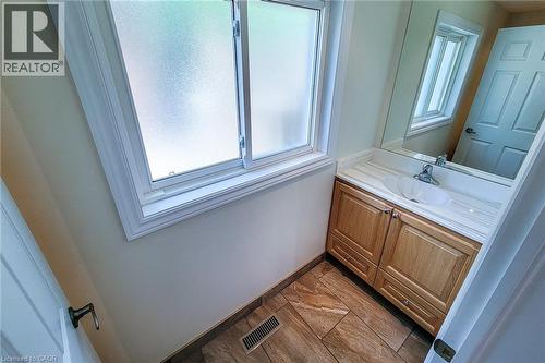 Frosted window providing privacy, wood-finish vanity with ample storage, integrated basin, reflective mirror, and tiled flooring - 319 King Street W, Dundas, ON - Indoor Photo Showing Bathroom