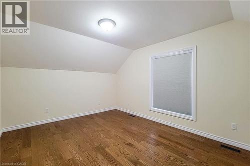 Room featuring rich wood-finish flooring, a contemporary ceiling light fixture, a window with a white frame, and sloped ceiling details - 319 King Street W, Dundas, ON - Indoor Photo Showing Other Room