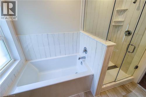 Bathroom featuring a white soaking tub with polished chrome fixtures, a clear glass shower enclosure with a built-in shelf, and wood-finish flooring - 319 King Street W, Dundas, ON - Indoor Photo Showing Bathroom