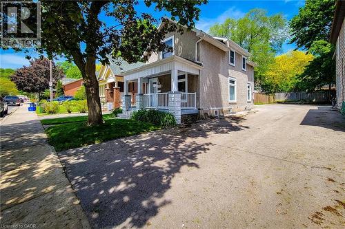 Two-story residence featuring a stucco exterior, covered front porch with white railings, multiple windows on both levels, a paved driveway, and a fenced rear boundary - 319 King Street W, Dundas, ON - Outdoor With Deck Patio Veranda