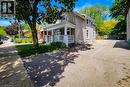 Two-story residence featuring a stucco exterior, covered front porch with white railings, multiple windows on both levels, a paved driveway, and a fenced rear boundary - 319 King Street W, Dundas, ON  - Outdoor With Deck Patio Veranda 