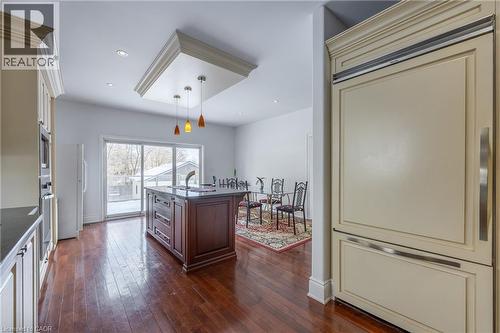 Spacious kitchen featuring a central island with integrated sink, rich wood-finish flooring, recessed lighting, and a custom panel-ready refrigerator - 514 Fishers Glen Road, Vittoria, ON - Indoor Photo Showing Kitchen