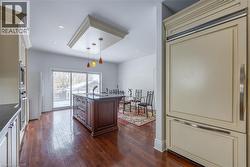 Spacious kitchen featuring a central island with integrated sink, rich wood-finish flooring, recessed lighting, and a custom panel-ready refrigerator - 